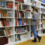 A young woman stands reading a book in a well-stocked library.